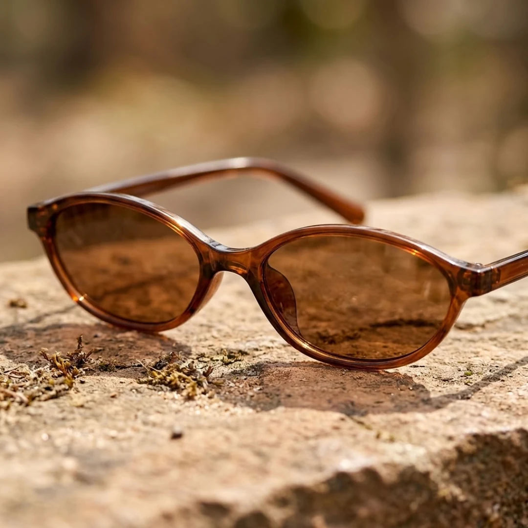 Detalhe da armação marrom translúcida e das lentes marrons do Mionelle Narrow Vibe Rich Brown sobre pedra