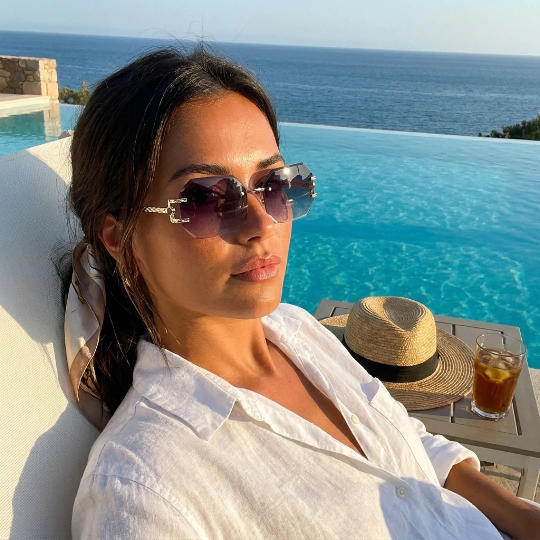 Mulher com os óculos Mionelle Facet Shadow Black à beira da piscina, com o mar ao fundo