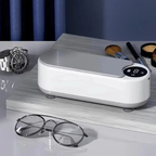 Limpador ultrassônico de óculos Mionelle Clair com tampa cinza sobre uma mesa e um par de óculos à frente.